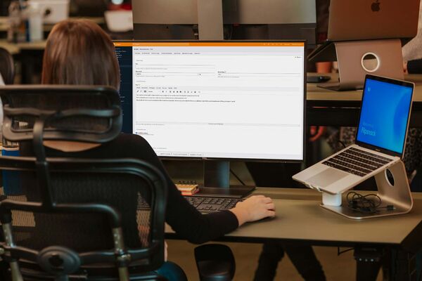 Eine Frau sitzt im Büro vor einem Computermonitor und arbeitet mit Contao